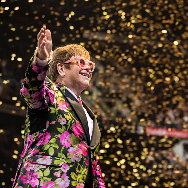 Elton John smiling onstage with glitter background